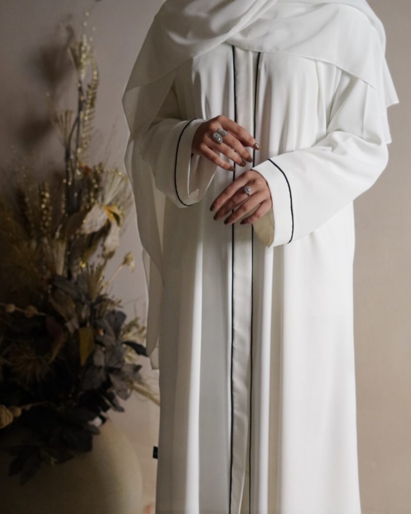 Graceful white abaya adorned with subtle piping accents, details, designed for comfortable and modest wear during umrah and Hajj rituals.